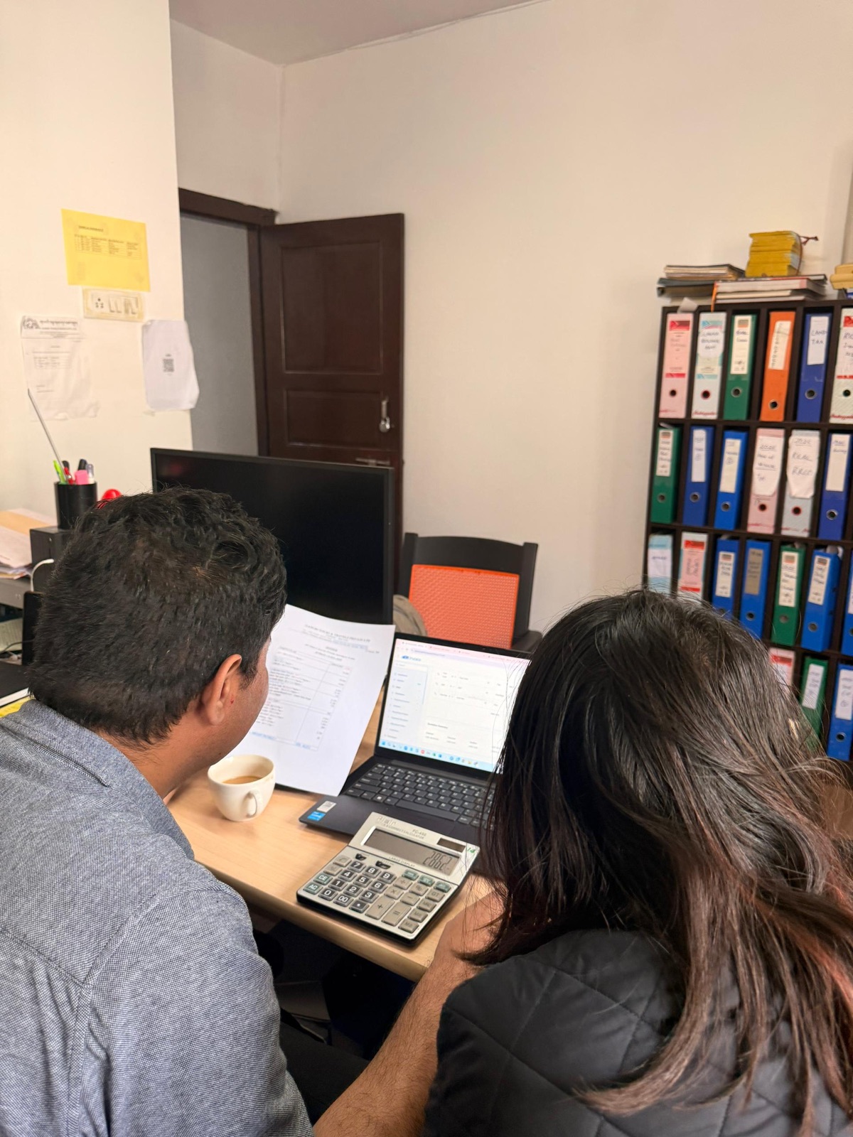 A Gangri Tours staff member reviewing a printed invoice next to aBit Invoice on the laptop.